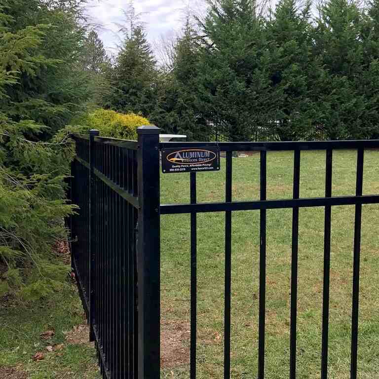 Black wholesale aluminum fence installed around a yard with trees in the background, featuring a company sign.